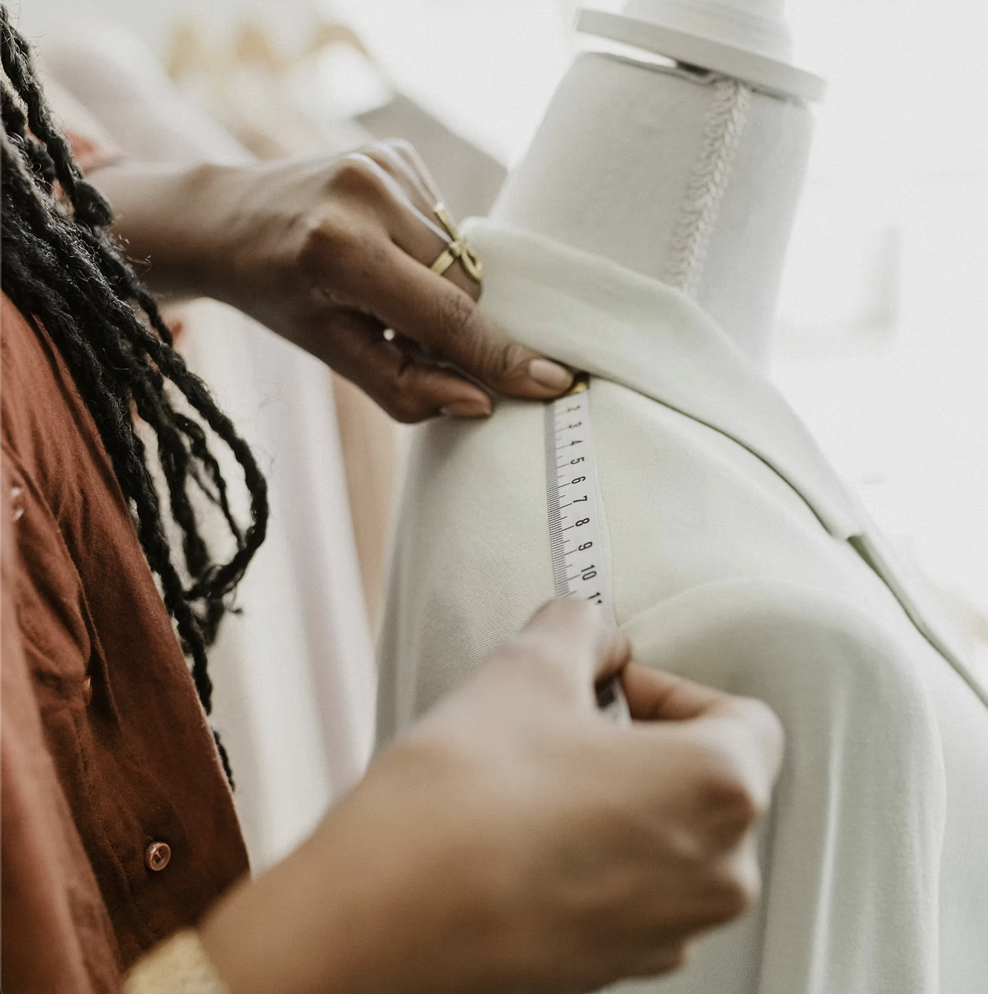 A maker measuring a garment on a dress form with a tape measure